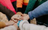 person in red sweater holding babys hand